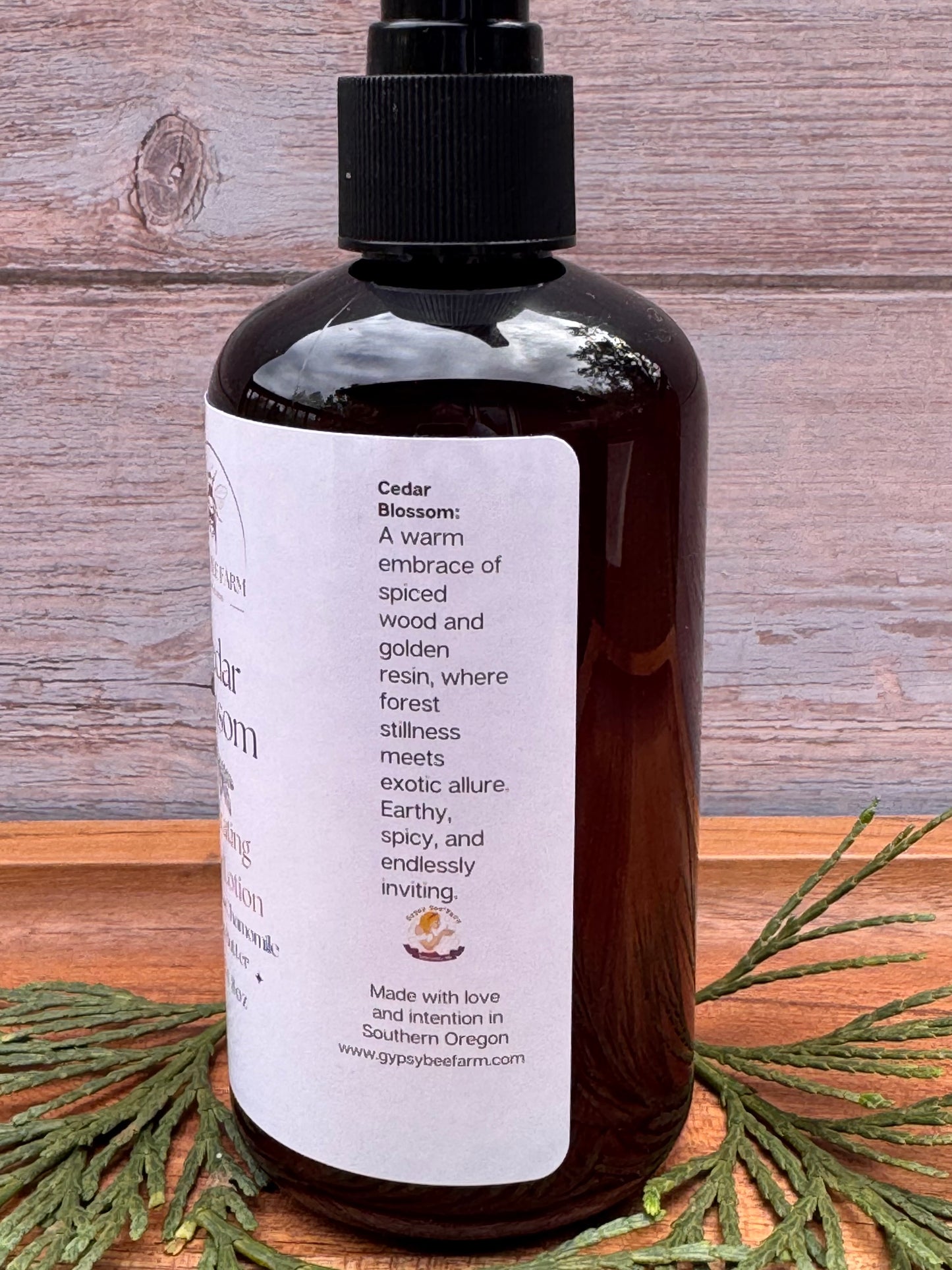 A bottle of cedar Blossom Lotion with cedar on a wooden board.