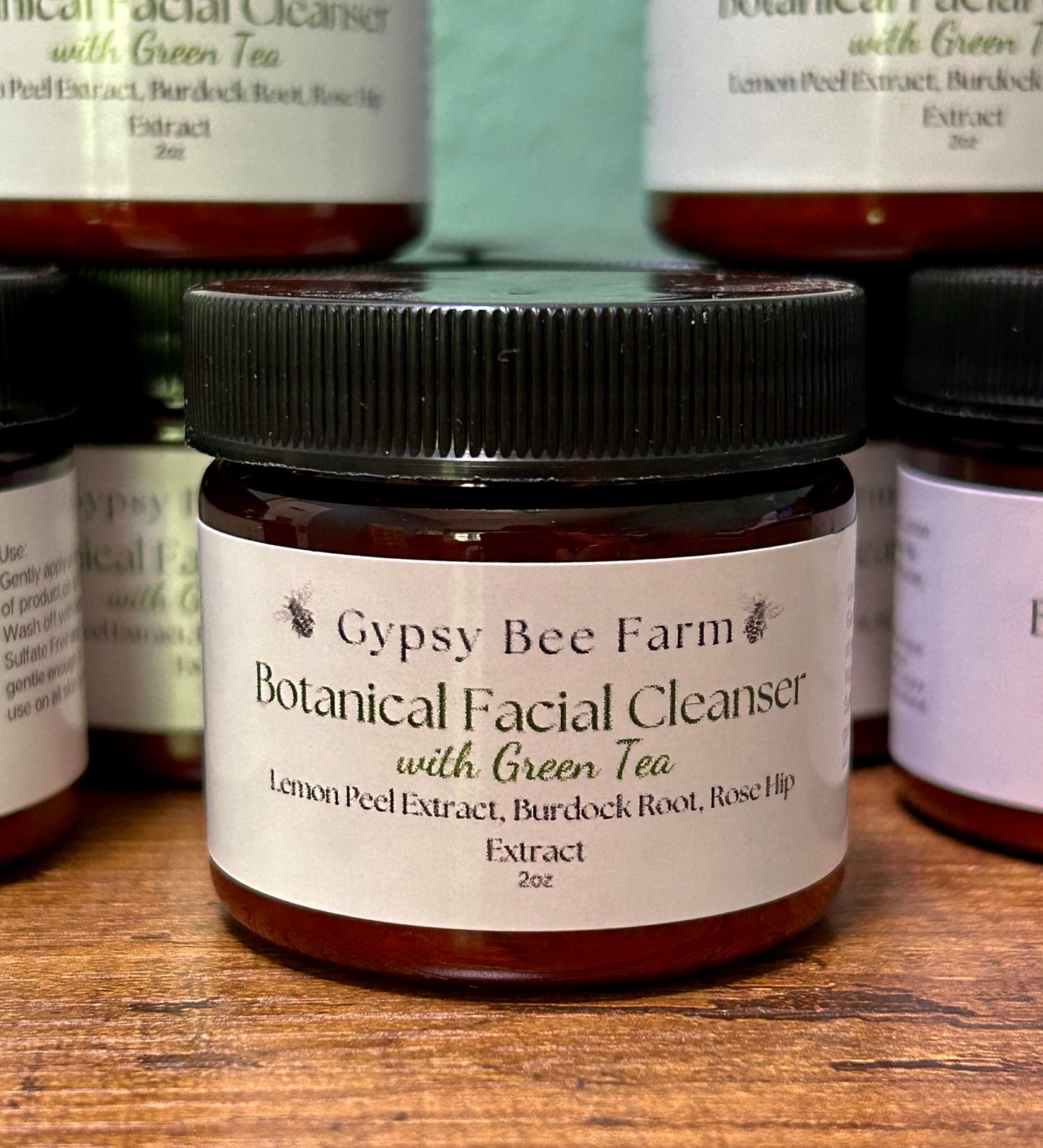 Jar of Gypsy Bee Farm Botanical Facial Cleanser with Green Tea on a wooden surface with other similar jars in the background.