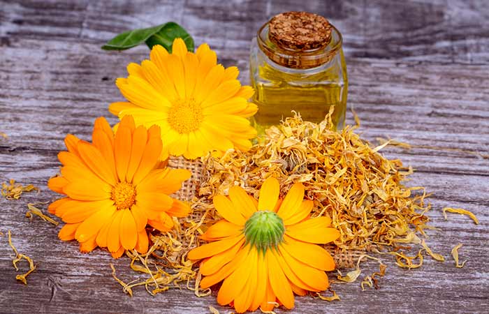 Calendula flowers and a jar of oil on a wooden surface