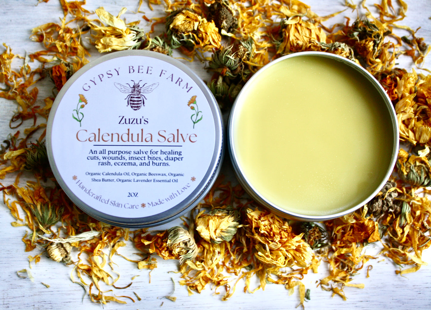 Gypsy Bee Farm calendula salve tin surrounded by calendula flowers on a wooden surface
