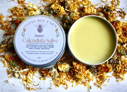 Gypsy Bee Farm calendula salve tin surrounded by calendula flowers on a wooden surface