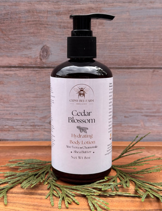 Bottle of Gypsy Bee Farm Cedar Blossom Hydrating Body Lotion on a wooden surface with greenery.