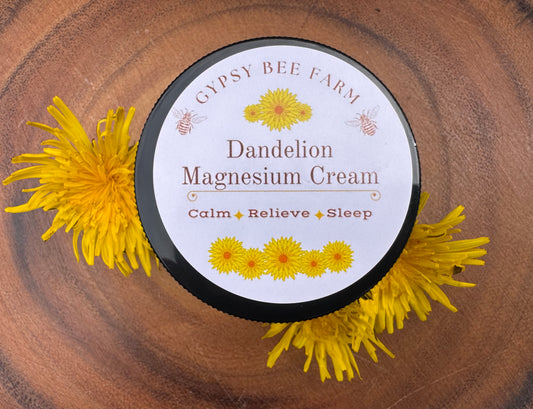 Gypsy Bee Farm Dandelion Magnesium Cream jar surrounded by dandelion flowers on a wooden surface