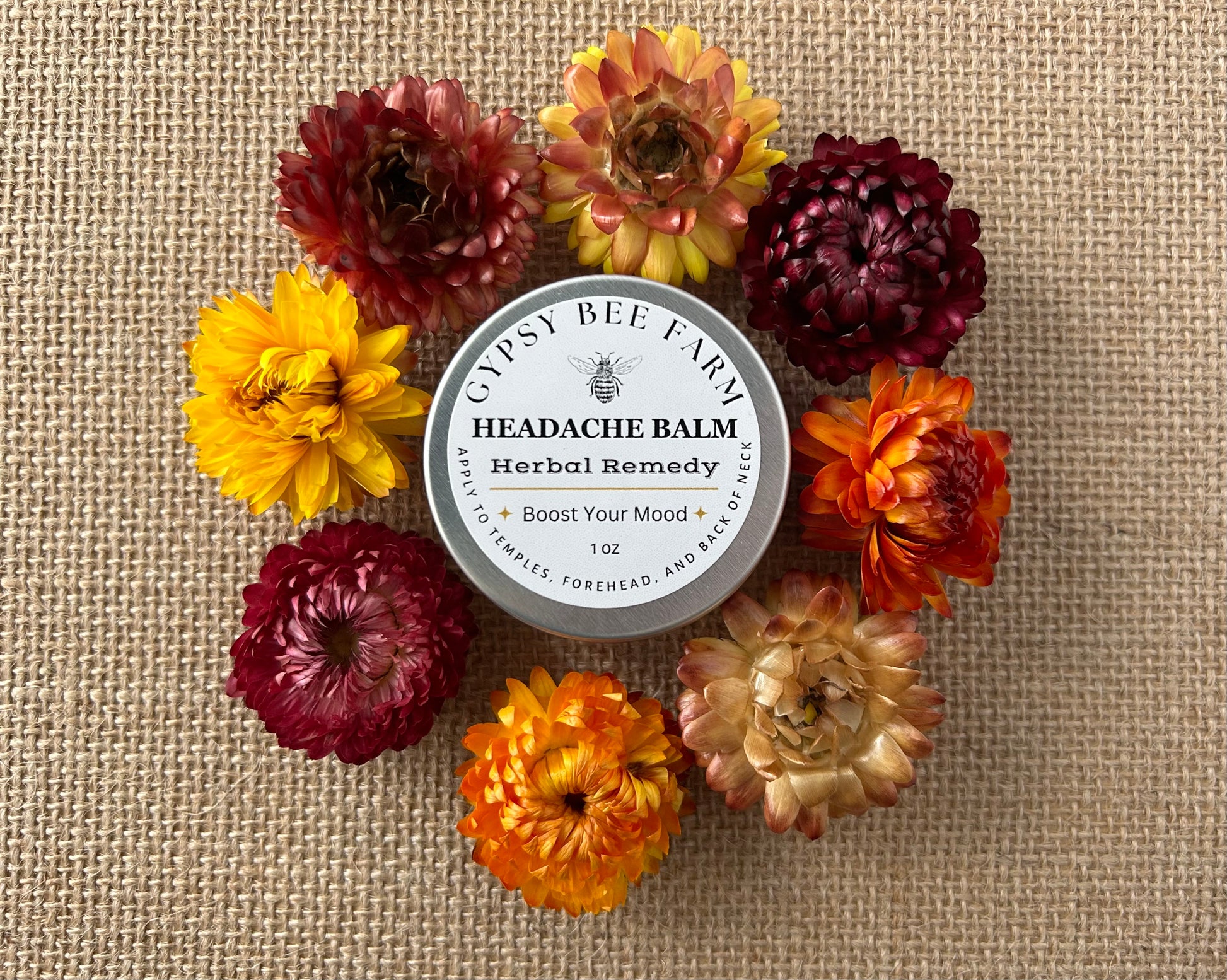 Headache balm container surrounded by colorful flowers on a textured fabric background