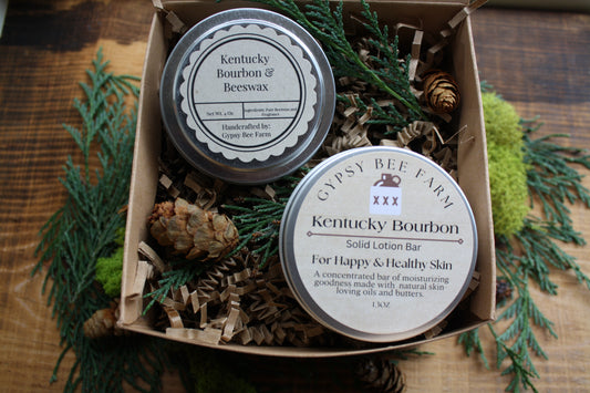 Two tins of 'Kentucky Bourbon' products in a box with greenery on a wooden surface