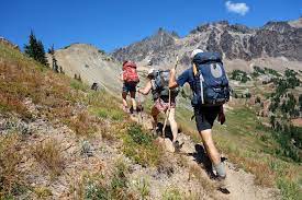 Hikers with backpacks on a mountain trail under a clear blue sky.