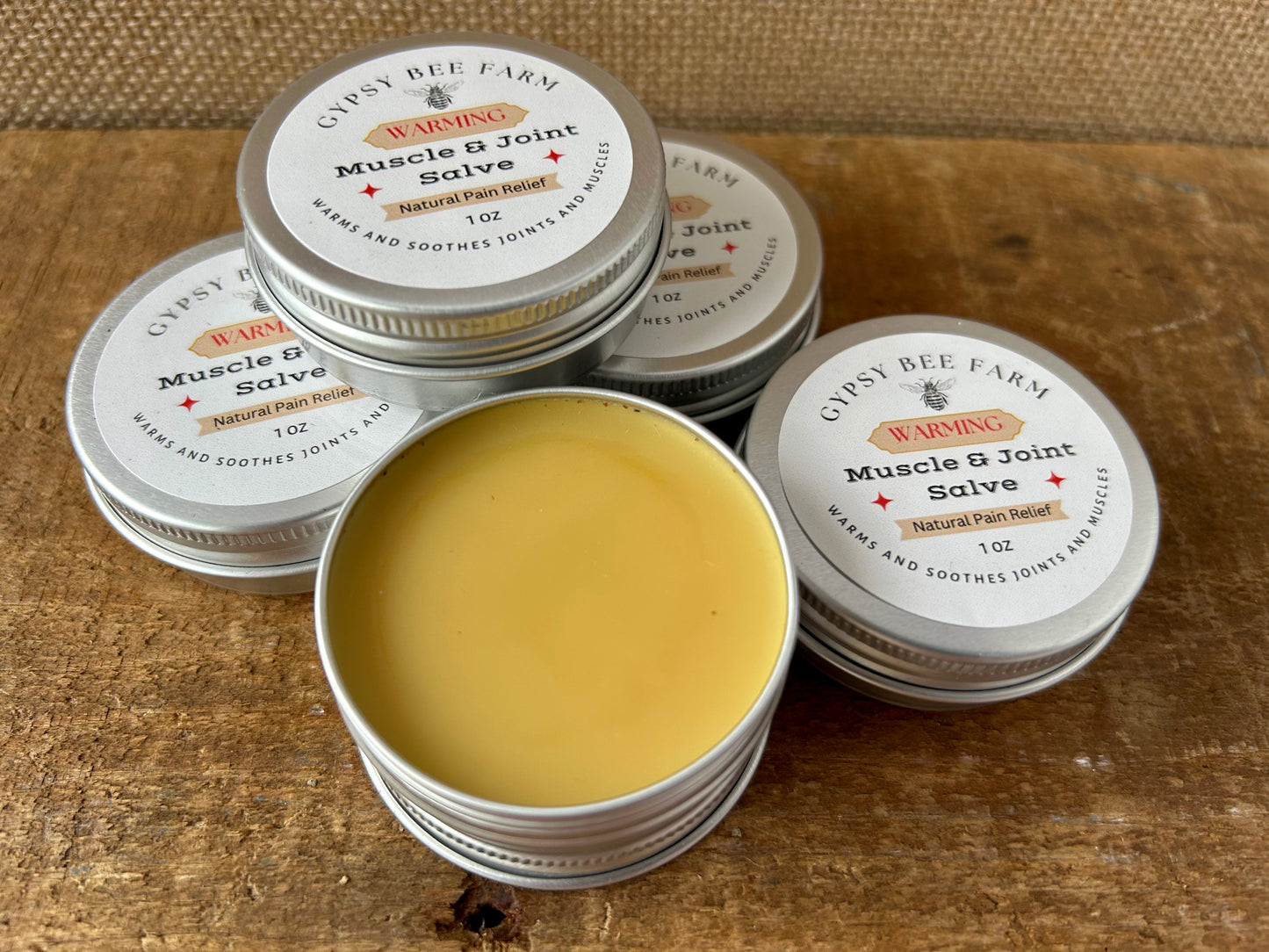Gypsy Bee Farm Muscle & Joint Salve tins on a wooden surface